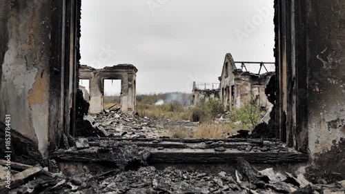 Dolly shot through a charred, broken window of a burnt-out building. Ruined architecture and desolate landscape after war or disaster. Aftermath of destruction
