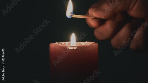 Hand lighting a candle with a match in a dark room at night