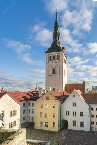 View of St. Olaf's Church steeple rising high above the colorful rooftops of the old town under a blue sky with clouds, Tallinn, Harju County, Estonia.