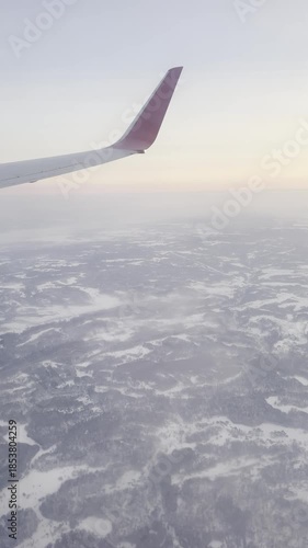 Airplane wing over winter landscape at sunrise from aerial view.