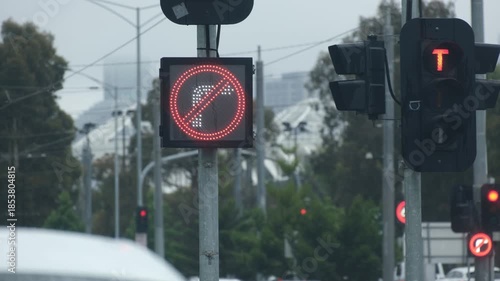 Illuminated traffic road signals indicating no right turn in Melbourne, Australia, viewed through a car with windshield wipers sweeping. Wet weather driving conditions and reduced visibility.