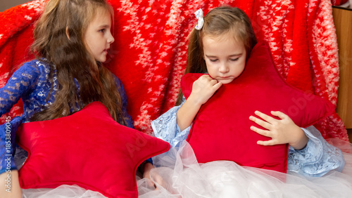 Two sisters in festive dresses sitting in the bedroom decorated with a Christmas tree and a garland