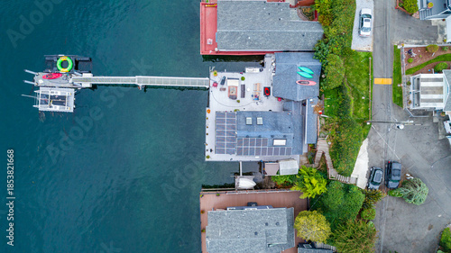 Aerial view of a house extending over the water with a dock, solar panels gleaming on the roof, and vibrant kayaks adding pops of color, Tacoma, Washington, United States.