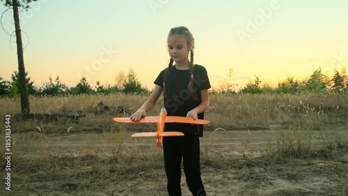 Girl play with toy airplane. Children toy plane in hands of child in summer in park under sun. Concept of child's dream of flying, child runs across field at sunset.
