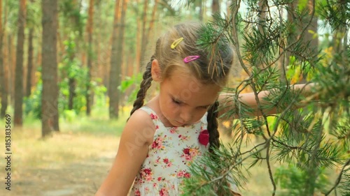 Caucasian child girl walking at a sunny forest. Kid feels positive while having fun in sunny green park. Brunette babe enjoying her vacation spend the weekend in the fresh air