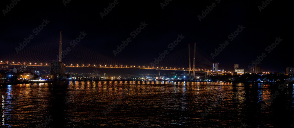 Fototapeta premium Modern Cable-Stayed Bridge at Night with City Lights and Water Reflection.