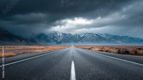 open road leading towards snow-capped mountains under a dramatic, stormy sky