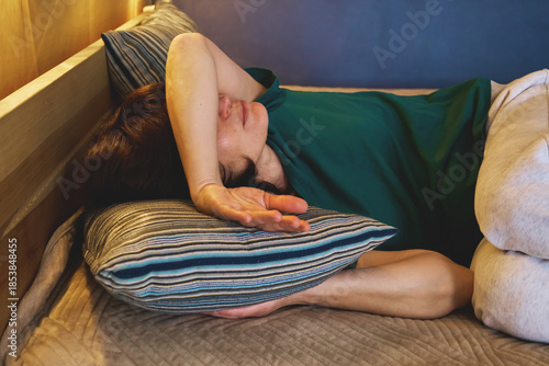 Woman lying in bed with her arm over her face, experiencing pain and discomfort