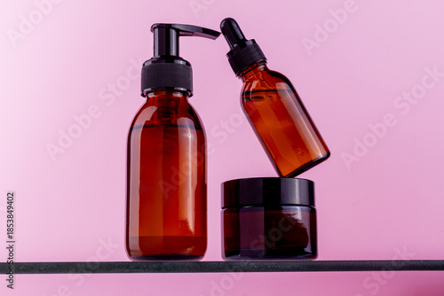 Amber glass cosmetic bottles and jar arranged on a shelf against a pink background