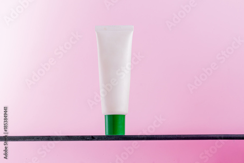 Minimalist white cosmetic tube with green cap on a pink background