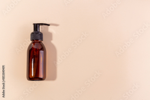 Amber glass pump bottle with black dispenser on a neutral background with shadow