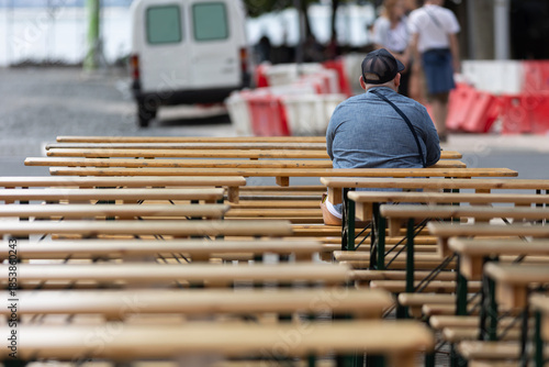 Person sitting alone on wooden bench during outdoor event
