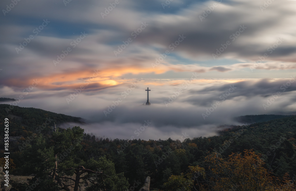 Obraz premium Cross rising above foggy forested landscape near Madrid