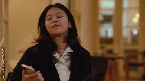 Stylish asian woman in formal black suit using modern smartphone and credit card while sitting at cozy cafe indoors. Business Woman enjoying convenience of online shopping.