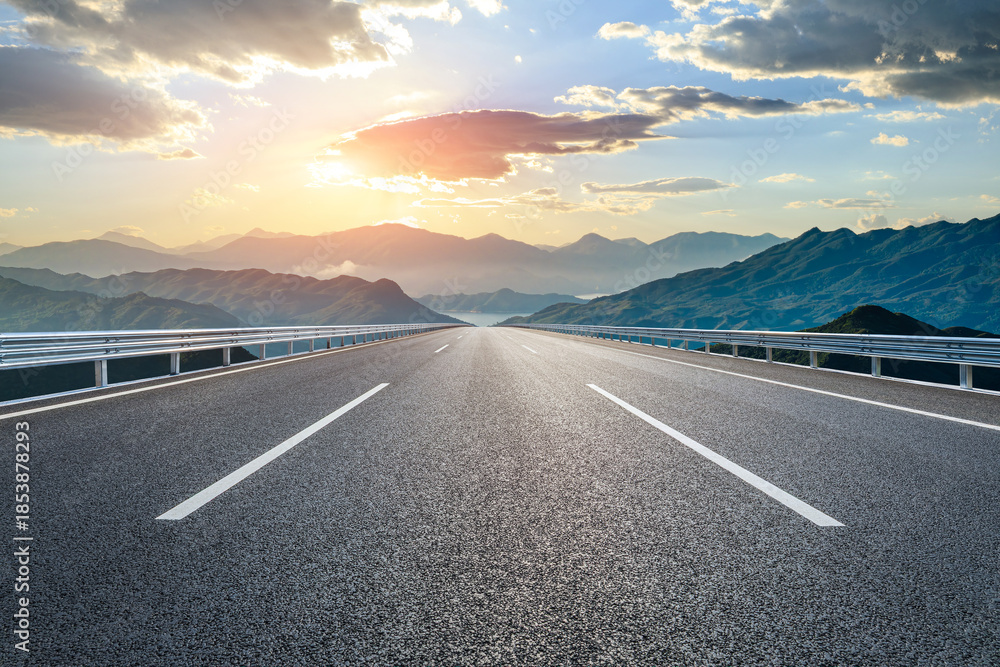 Fototapeta premium Empty asphalt highway road leading towards the distant mountain range at sunset