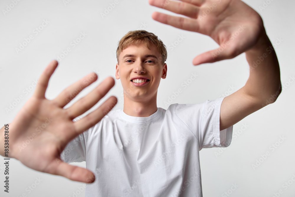 Fototapeta premium Hands, smile, young, man, framing, forward, whiteshirt, playful composition open gesture friendly mood in studio setting with bright light for casual lifestyle and youth engagement