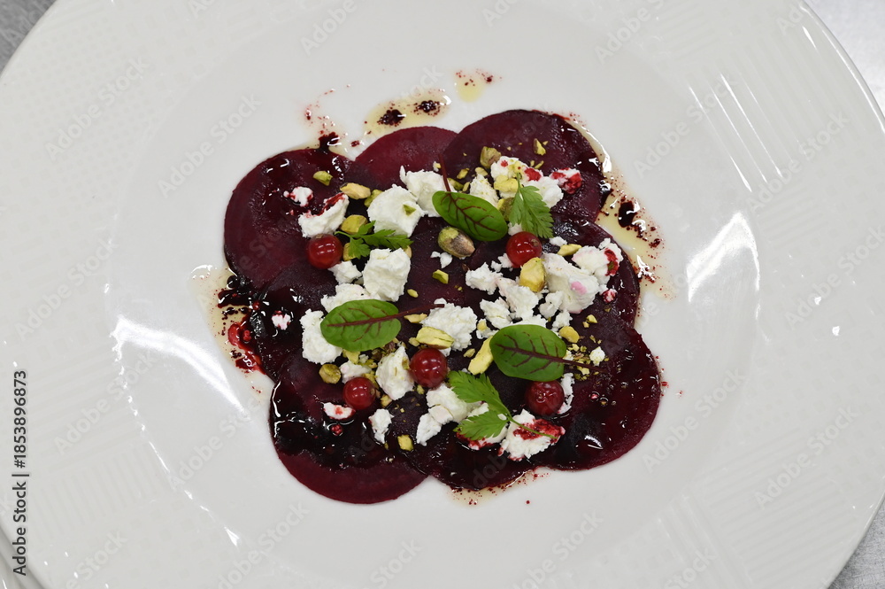 Fototapeta premium sliced beetroot appetizer with goat cheese and fresh herbs, close-up view, served on a white plate, modern restaurant cuisine,