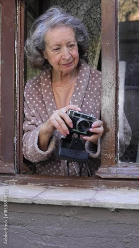 Nosy senior woman filming the neighbours through the window 