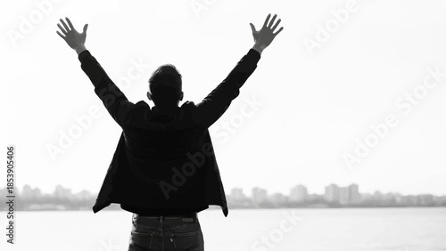 A silhouette of a man with his arms raised in triumph by the water