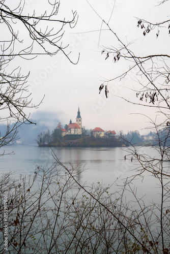 Misty winter landscape with small island featuring historic church surrounded by calm lake waters