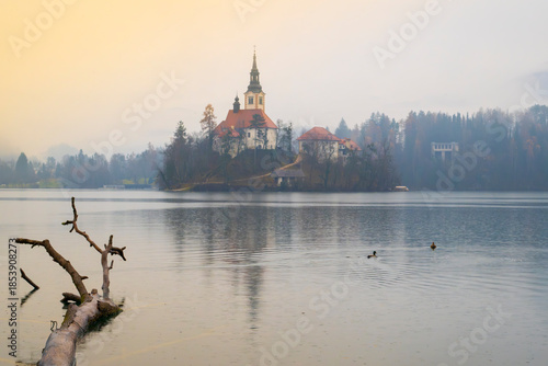 Misty morning scene of historic church on a serene island surrounded by calm lake waters and forest