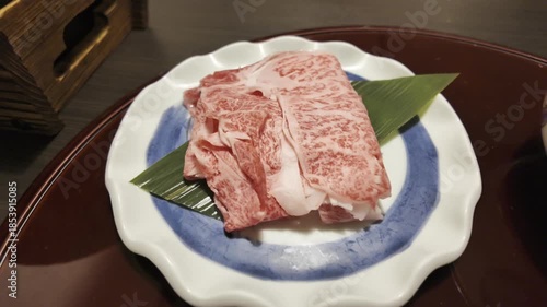 Several slices of bright red beef with beautiful marbling are placed on an exquisite plate.