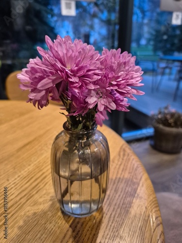 A purple chrysanthemum stands on a table in semi-darkness.