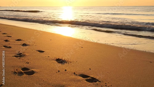 Footprints in the sand leading to the ocean at sunrise.