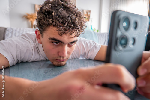 Young man engrossed in phone screen, exhibiting boredom and technology addiction symptoms, possibly procrastinating