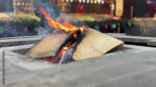 Open fire burning on wooden logs at an outdoor winter market, creating warm, cozy atmosphere.