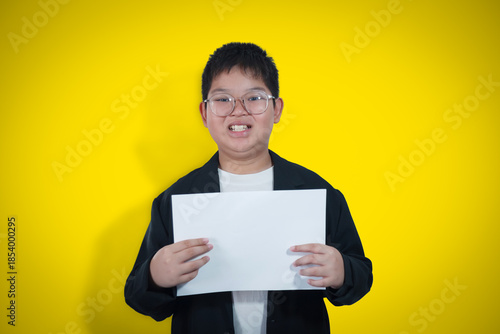 A boy in a business suit holds a white sheet of paper against a yellow gold background.