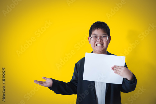A boy in a business suit holds a white sheet of paper against a yellow gold background.