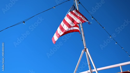 American flag waving on New York harbor. The American flag flutters above a cruise boat in the New York harbor with blue sky