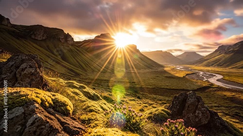 The sun rises over the mountains, casting rays of light across the lush valley. This vibrant valley features colorful flowers and a winding river that enhance the beautiful landscape.