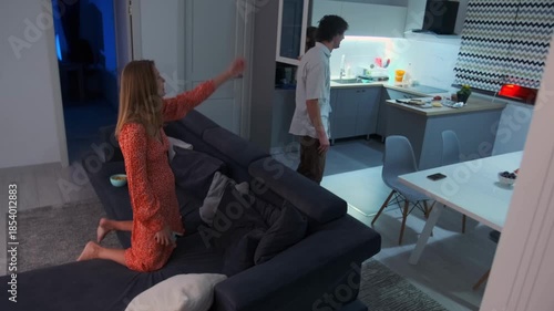 white woman pointing at doorway insisting departure man moving sofa through living room late night tension packed furniture urgent gestures emotional confrontation roommate split dramatic interior