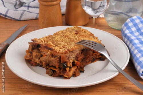 Part de lasagnes aux légumes maison servie dans une assiette avec une fourchette en gros plan servie à table avec un verre d'eau