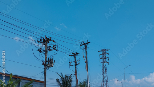 Electric power poles and transmission lines against clear blue sky in urban area. Energy infrastructure, electricity distribution, power supply, technology, industry and city development concept