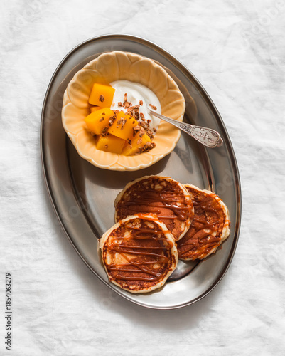 Delicious breakfast, brunch - pancakes with caramel sauce, yogurt with granola and mango on a light background, top view