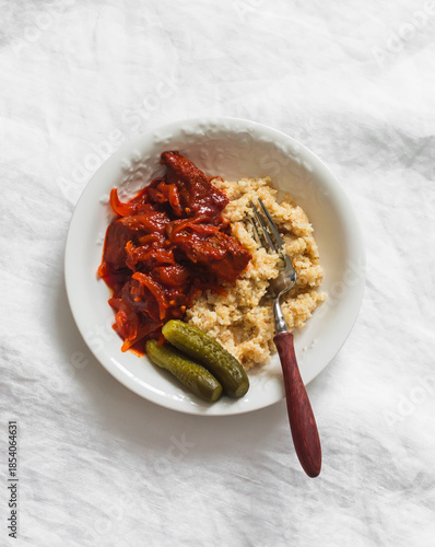 Beef stew in tomato sauce, wheat porridge, pickled cucumbers - a delicious lunch on a light background, top view