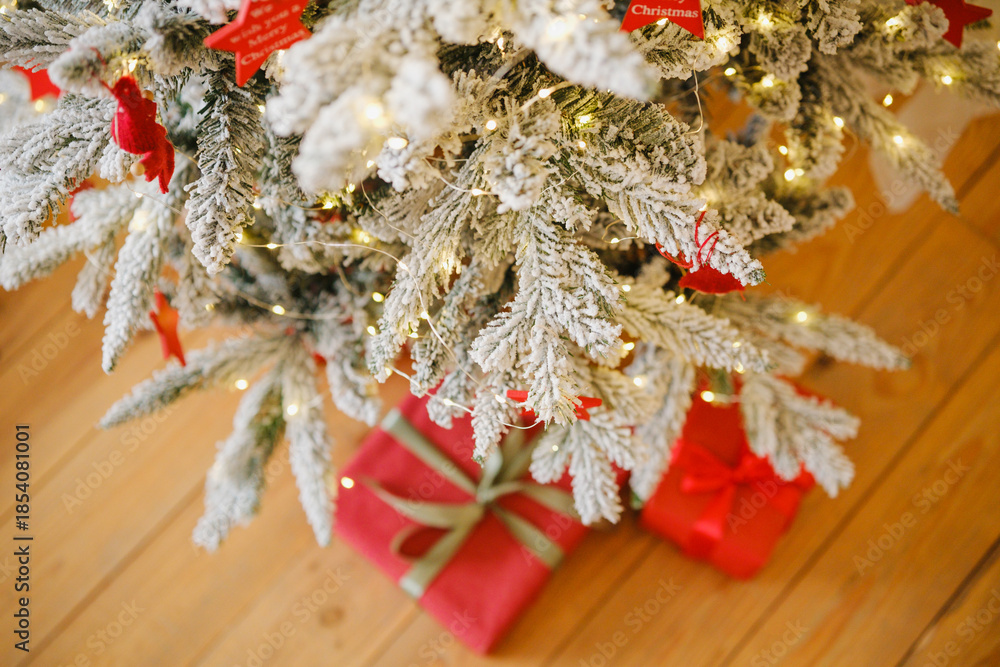 Fototapeta premium Frosted Christmas tree branches with warm lights and red gift boxes below on wooden floor