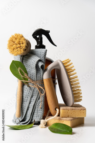 Zero Waste Eco Cleaning Concept with Wooden Brushes, Reusable Glass Dispenser and Green Leaves on White Background with Copy Space