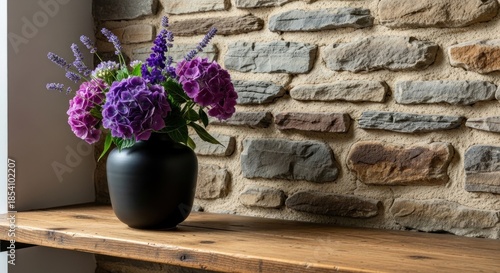 A vase of purple flowers on a wooden shelf against a stone wall.