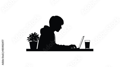 Silhouette of a person working on a laptop at a desk with a plant
