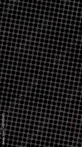 Close up of a dark metal speaker grill with round holes