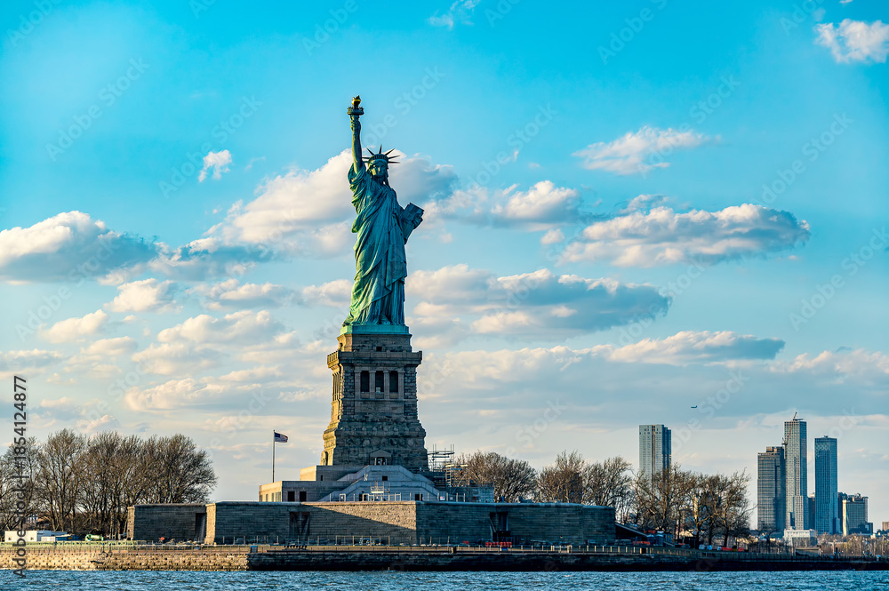 Fototapeta premium Statue of Liberty with blue sky in the background. The Statue of Liberty stands with the blue sky and white clouds behind it.