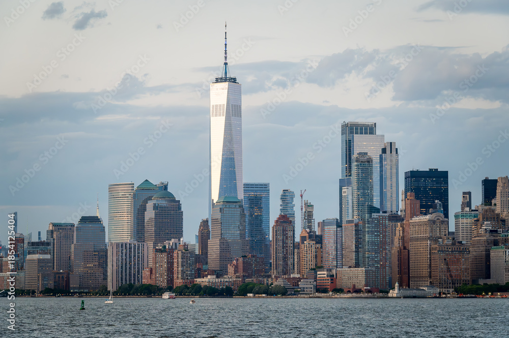 Obraz premium Manhattan skyline with One World Trade Center under cloudy sky. View of Manhattan skyline with One World Trade Center and surrounding skyscrapers under a cloudy sky.