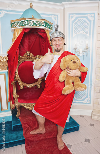 Confident funny smiling man wearing medieval costume showing thumbs up and holding teddy bear