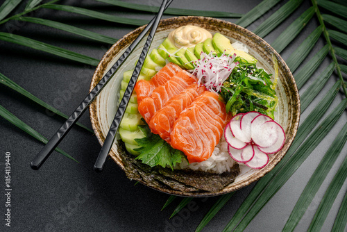 Salmon Poke Bowl with Colorful Toppings and Creamy Sauce. An elevated perspective captures a salmon poke bowl with sliced salmon, avocado, radish, and seaweed, arranged with a creamy sauce dollop.
