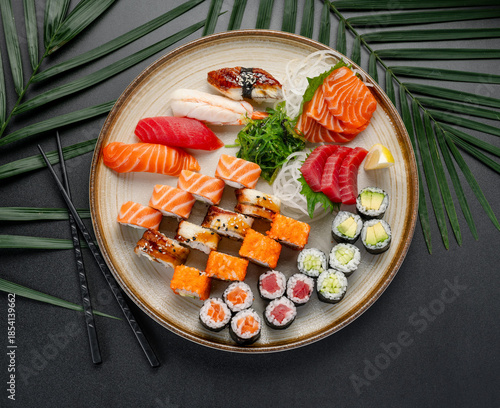 Assorted Sushi, Sashimi, and Rolls Platter on Dark Background. A large platter features a diverse assortment of sushi, sashimi, and maki rolls arranged elegantly on a textured plate.