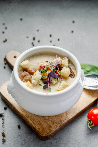 Bowl of Creamy Mushroom Soup with Croutons and Herbs. A white bowl of creamy mushroom soup is beautifully garnished with sliced mushrooms, croutons, and fresh purple herbs.
